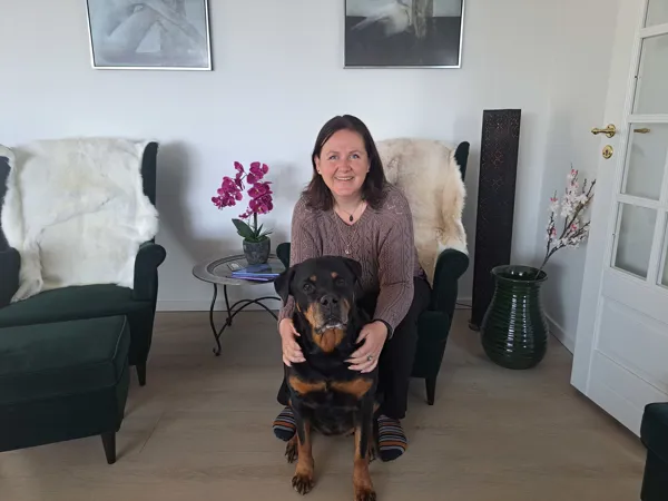 Kvinde sidder i stol, med sin hund på gulvet foran