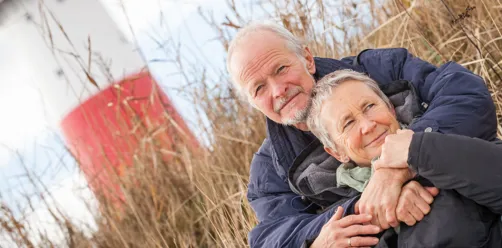 Kvinde og mand sidder ved en strand med siv i baggrunden.