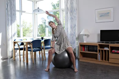 En kvinde sidder og udfoerer balanceoevelser på en bold.