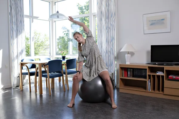 En kvinde sidder og udfører balanceøvelser på en bold.
