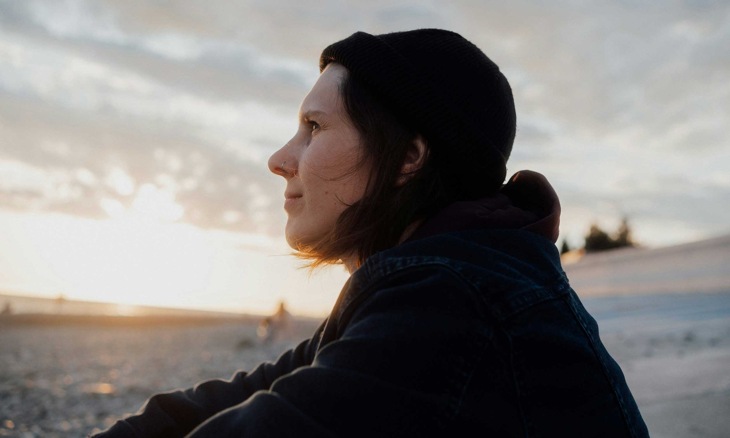 Kvinde sidder ved en strand ved solnedgang en kølig aften 