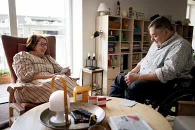Paaroerende snakker med mand i koerestol i dagligstue