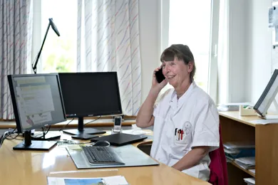 Laege sidder ved bord og snakker i telefon