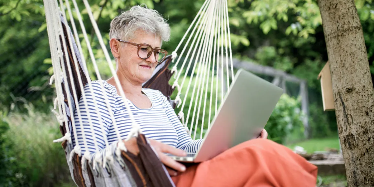 Kvinde sidder med computer udenfor i en haengekoeje.