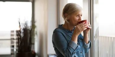 Kvinde drikker kaffe og kigger ud af vinduet.
