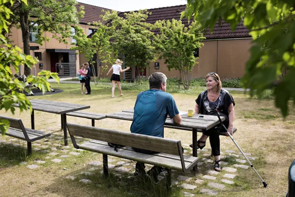 En kvinde taler med en mand på en baenk over en kop kaffe