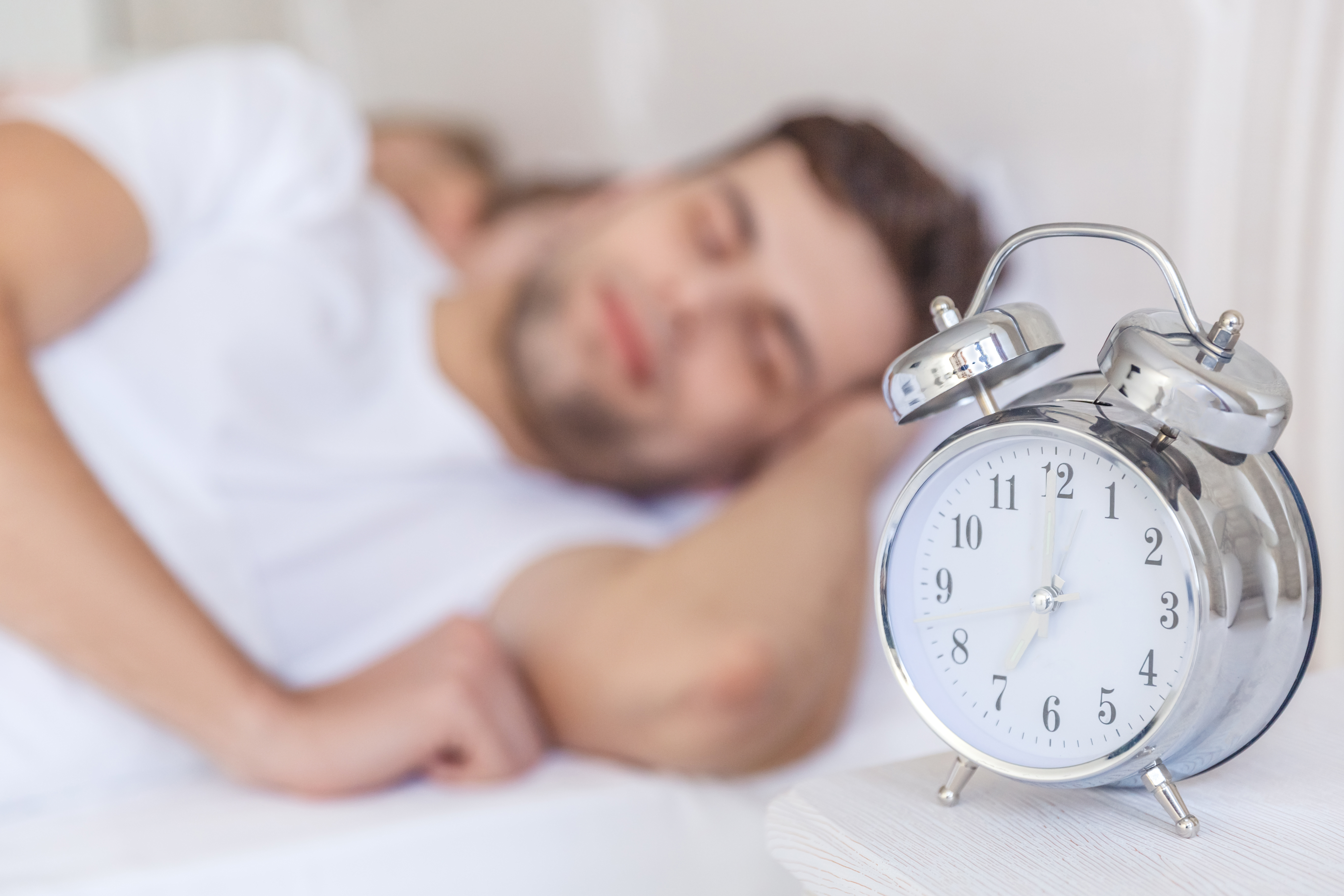 Mand ligger og sover ved siden af et vækkeur.