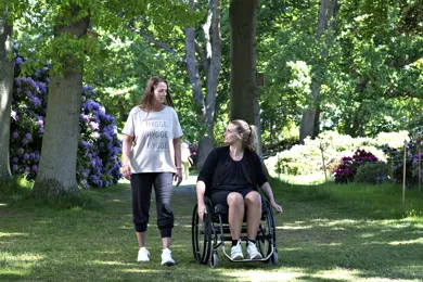 En ulykkesramt i en koerestol med en hjaelper ved sin side.