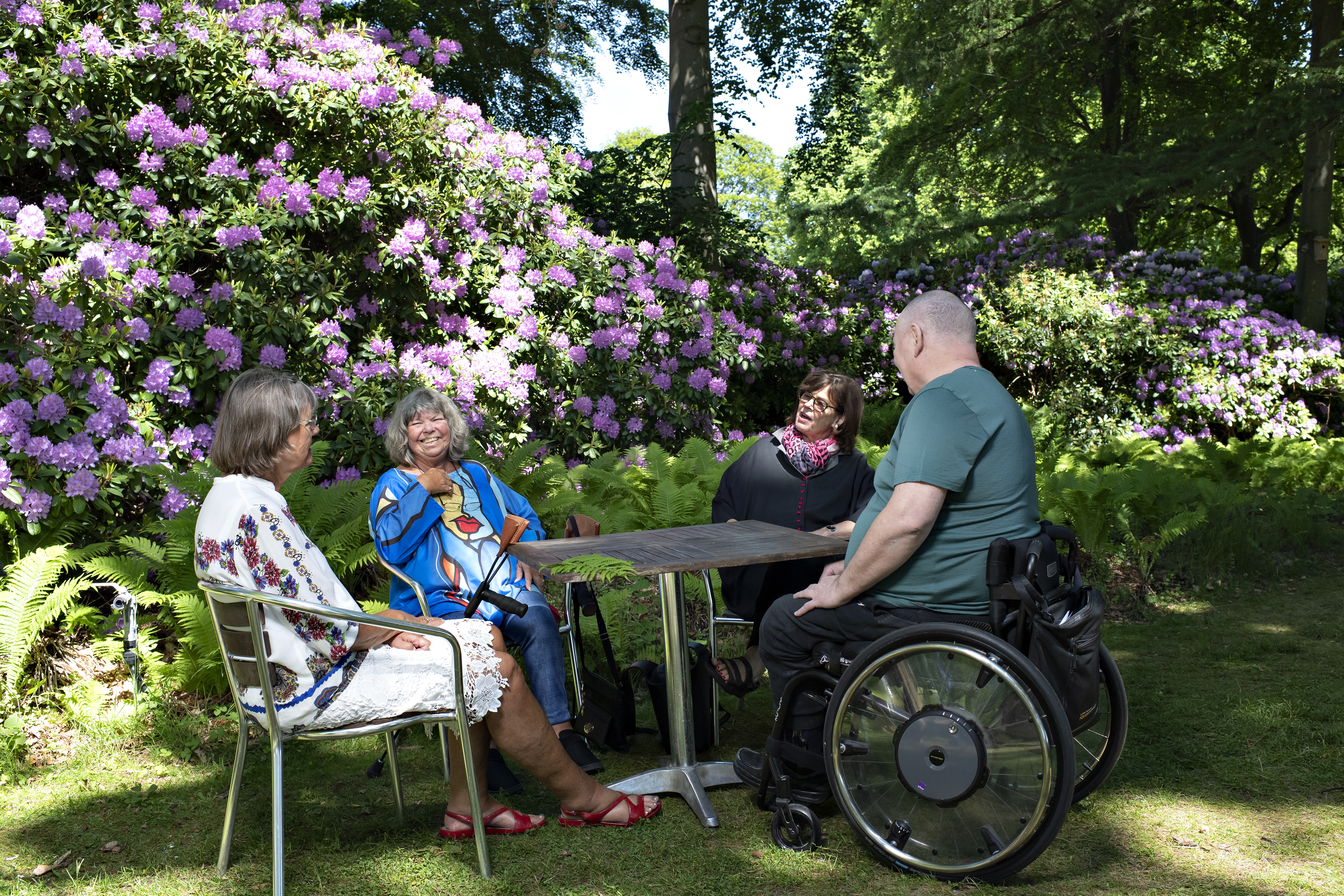 Fire personer sidder ved et bord og taler ude i naturen.