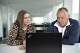 To personer sidder og taler sammen foran en computer