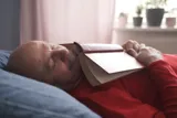 En mand er faldet i søvn i sin seng, mens han lå og læste en bog.